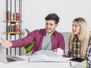 Young adults studying together, smiling and using a laptop.